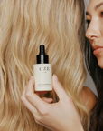 Model holding CZE Hair Nourishing Perfume Oil next to healthy blonde hair – lightweight and hydrating hair oil